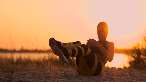 Junge-Schöne-Sportlerin,-Die-Am-Strand-Bei-Sonnenuntergang-Übungen-Für-Die-Bauchmuskulatur-Macht-Und-Sich-In-Zeitlupe-Dreht